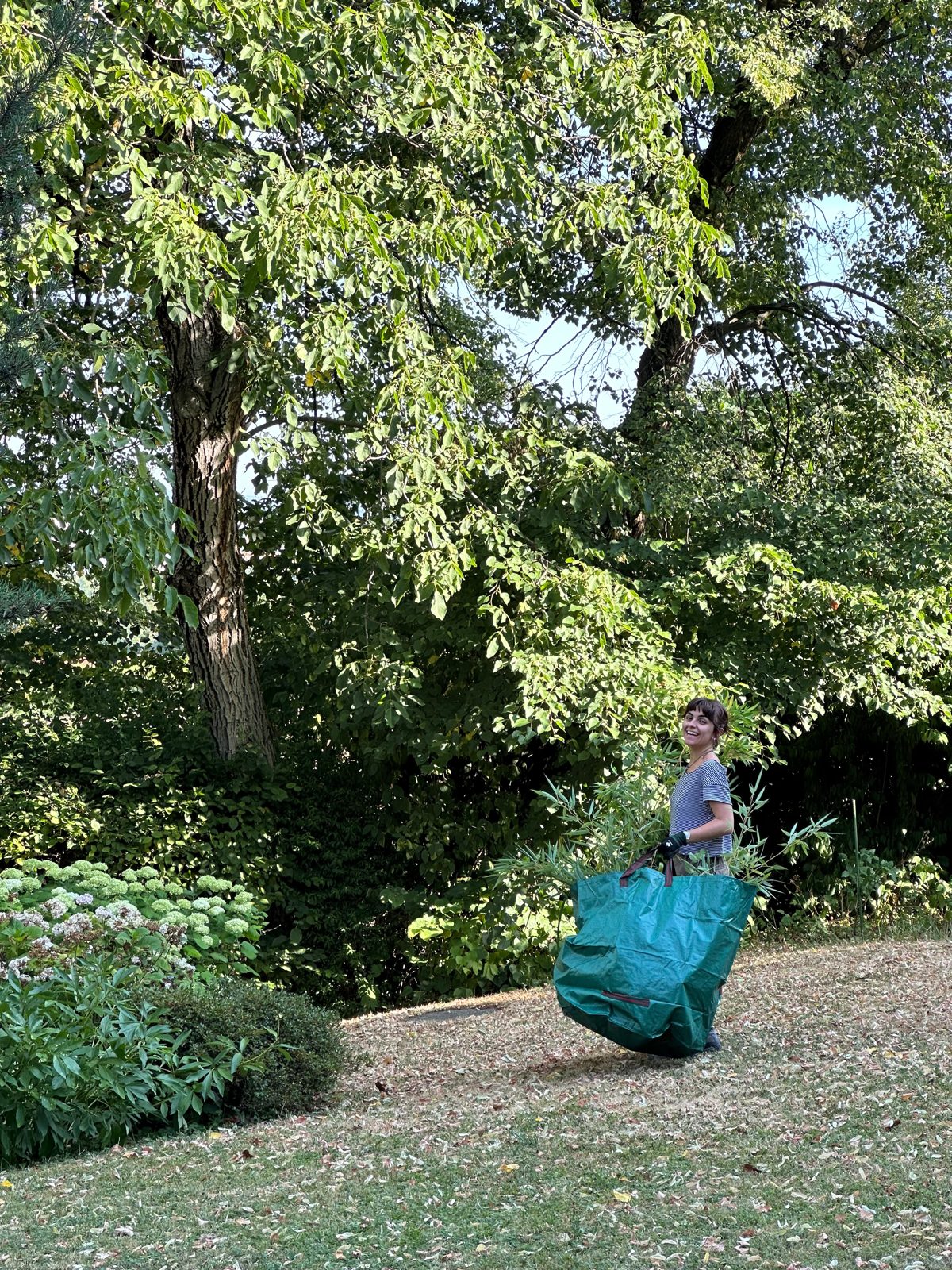 Studentin trägt einen gefüllten Gartensack durch einen Garten